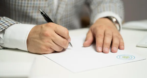 A person in a checked jacket signing a document with a pen